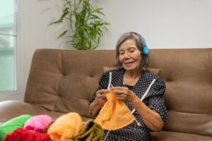 Older woman knitting with headphones on.