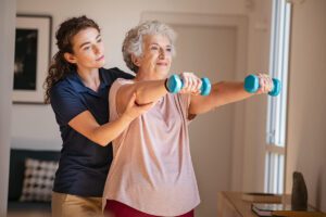 Caregiver helping an older woman raise a pair of dumbbells